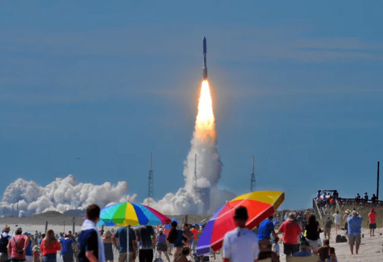 Vibrant rocket launch seen from Cape Canaveral’s beaches with colorful umbrellas in the foreground.