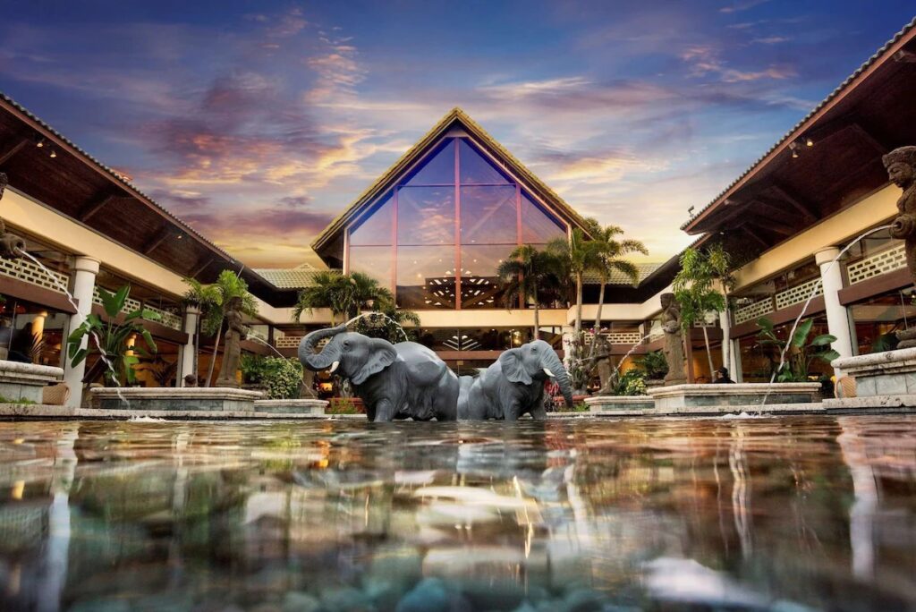 Entrance of Loews Royal Pacific Resort at Universal Orlando, showcasing its tropical theme with lush palm trees and a serene water feature.