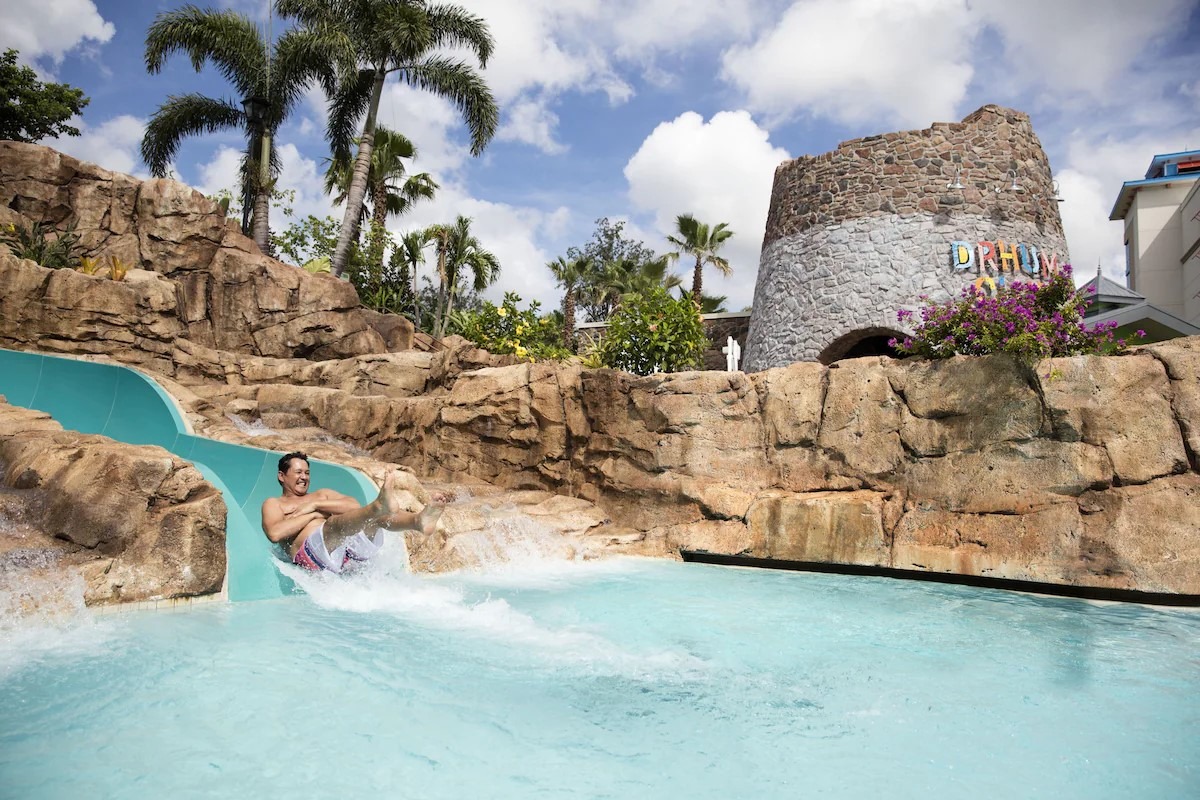 Guest enjoying a water slide at Loews Sapphire Falls Resort pool surrounded by lush tropical landscaping at this favorite Universal Studio hotels in Orlando.