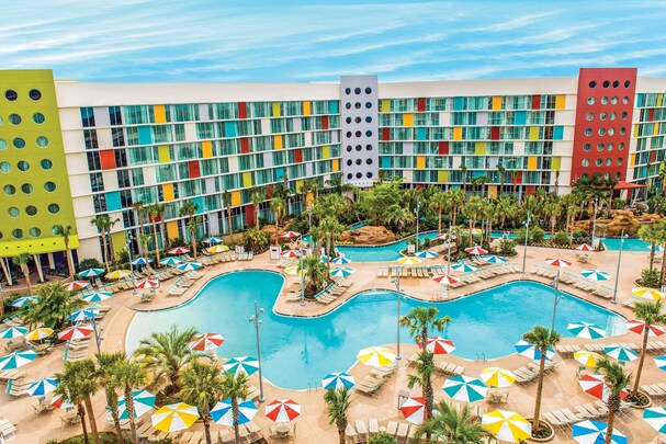 Cabana Bay Beach Resort pool area with colorful umbrellas and lounge chairs, vibrant hotel facade in the background, and a relaxing tropical ambiance at one the top Universal Studio hotels in Orlando, Florida.