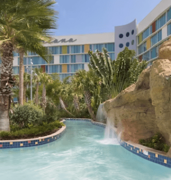 A serene lazy river winding through a lush tropical landscape with palm trees, cascading waterfalls over rocks, and the colorful façade of a favorite Universal Studio hotels in Orlando, Florida