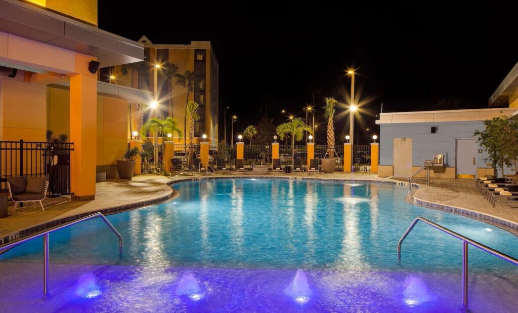 Hyatt House at Universal Orlando's pool area illuminated at night, featuring a stylish, curved pool with underwater lighting.