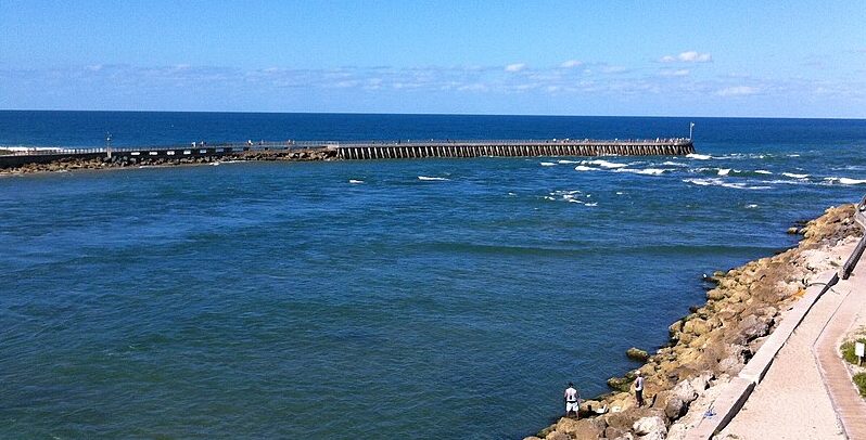 View of Sebastian Inlet State Park featuring the inlet, a jetty, and people fishing along the rocky shore.