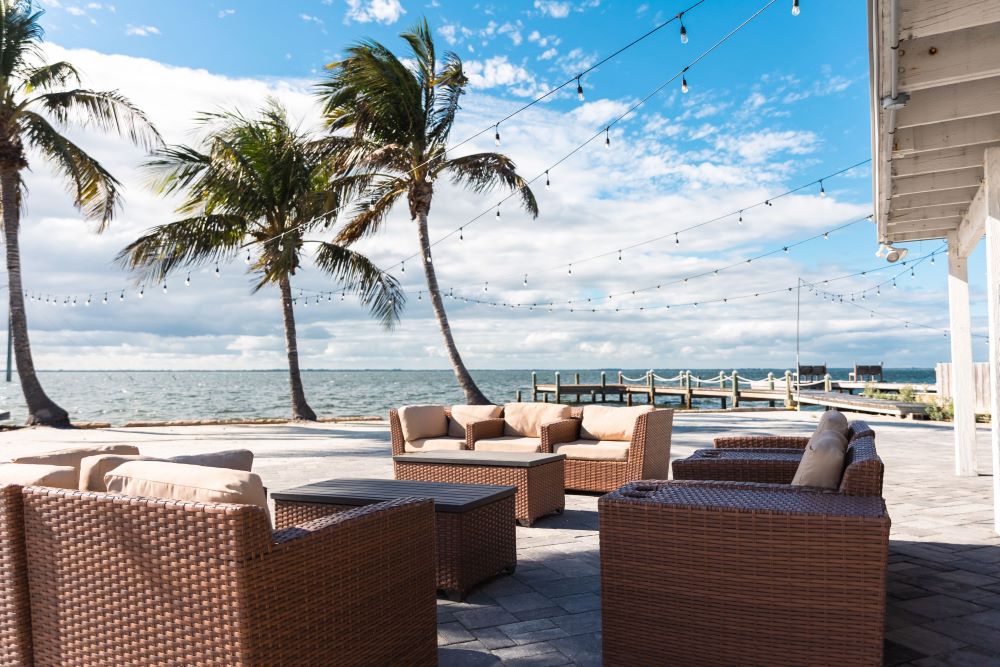 Scenic view of a tropical resort by the Banana River featuring palm trees, oceanfront seating, and a luxurious patio setup.