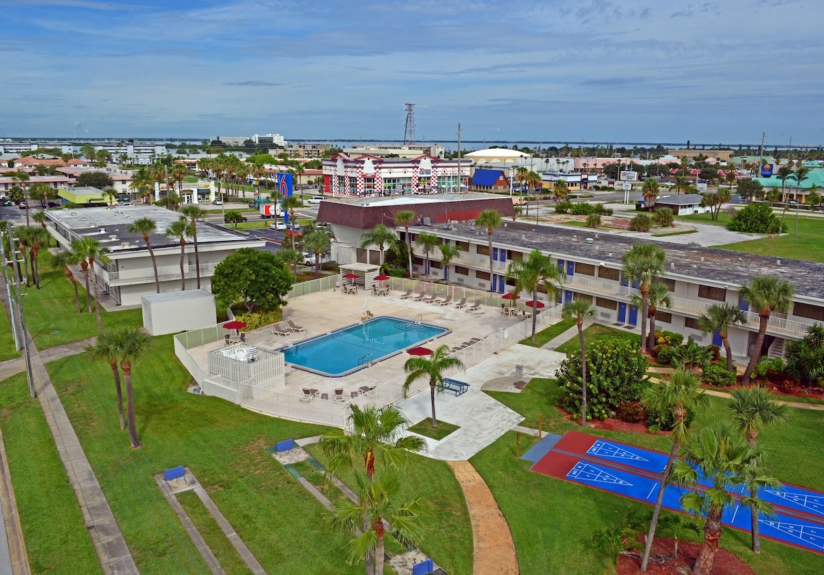 Aerial view of the pet friendly Motel 6 Cocoa Beach featuring an outdoor pool, shuffleboard courts, and budget-friendly accommodations.