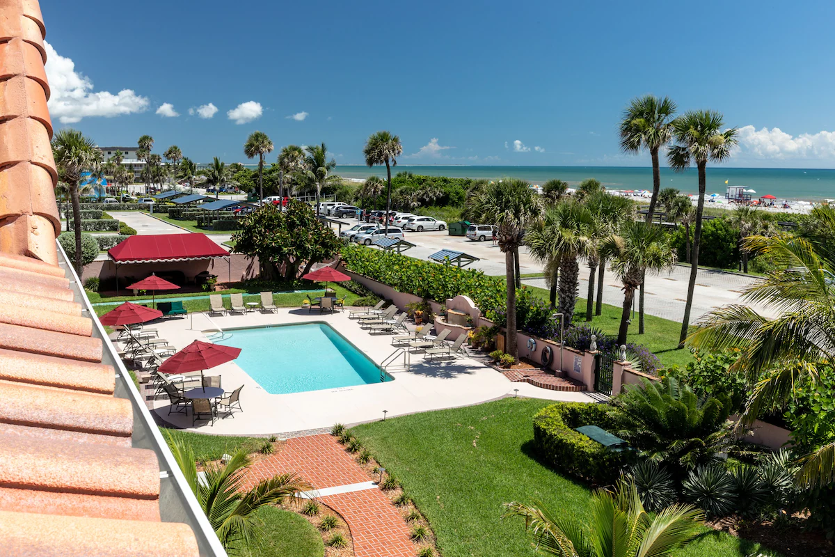 Exterior view of the Inn at Cocoa Beach featuring a pool, lush gardens, and ocean views.