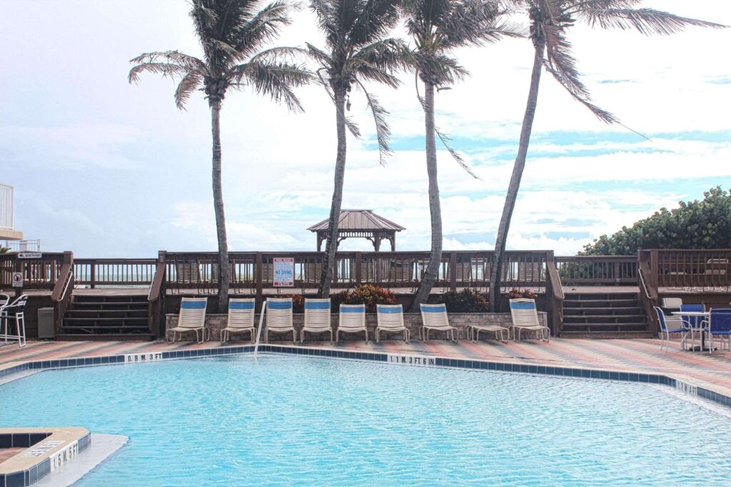 Swimming pool area at Radisson Suite Hotel Oceanfront with palm trees and lounge chairs.