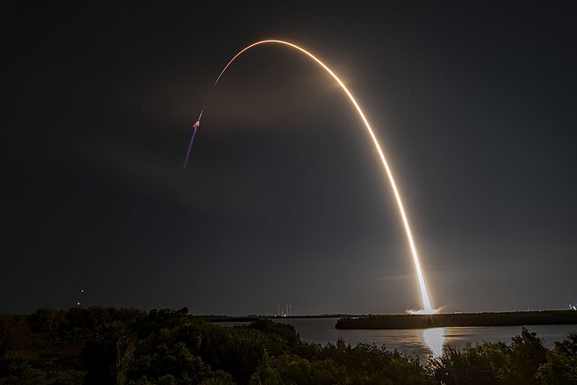 SpaceX Falcon 9 rocket launching at night from Kennedy Space Center, creating a golden streak in the sky on Florida's Space Coast.