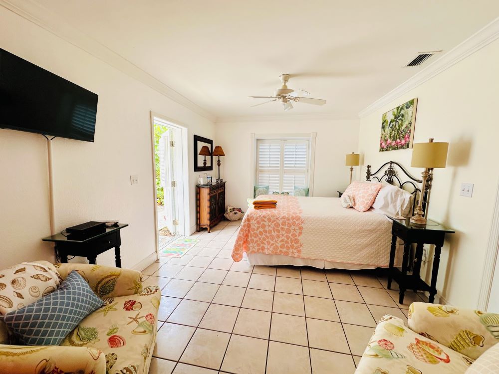 Interior view of a cozy guest room at Windermere Inn by the Sea, featuring a bed, TV, and tropical decor.