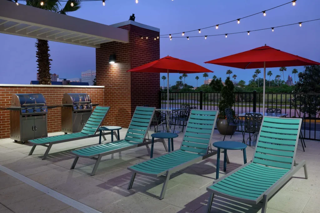 Outdoor seating area with lounge chairs at Home2 Suites by Hilton near Universal Orlando, featuring palm trees and sunny weather