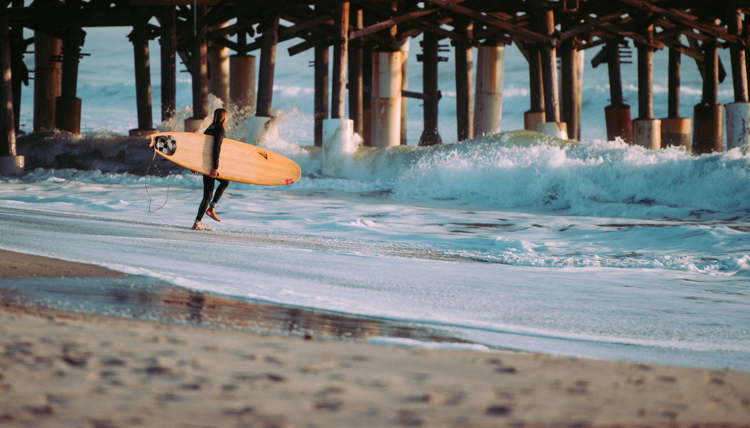 Surfer walking into the Atlantic Ocean near Cocoa Beach Pier with beachfront hotels in the background