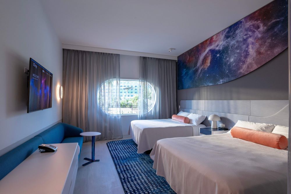 Guest room at Universal Stella Nova Resort near Epic Universe, featuring two queen beds, cosmic galaxy mural, modern decor, and space-themed ambiance